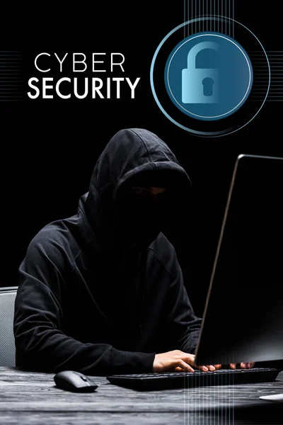 Hacker sentado cerca del monitor de la computadora y escribir en el teclado de la computadora cerca de letras de seguridad cibernética en negro - foto de stock