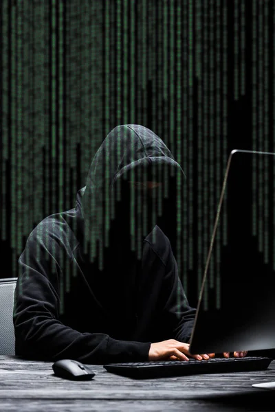 Hacker en la máscara sentado cerca del monitor de la computadora y escribir en el teclado de la computadora cerca de la ilustración en negro - foto de stock