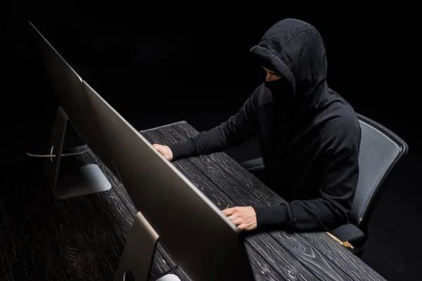 Hooded hacker in mask attacking network isolated on black — Stock Photo