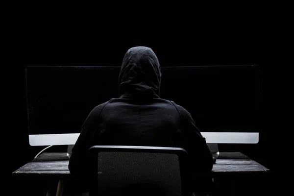 Visão traseira do hacker sentado perto de monitores de computador com tela em branco isolado em preto — Fotografia de Stock