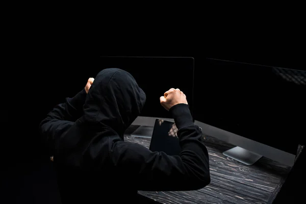 Upset hacker with clenched fists near computer monitors with blank screen isolated on black — Stock Photo