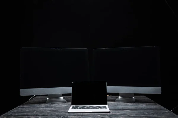 Portátil con pantalla en blanco cerca de monitores de ordenador aislados en negro - foto de stock