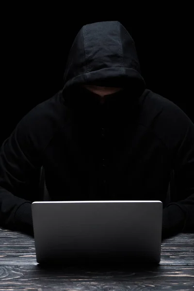 Hacker anônimo no capuz usando laptop isolado em preto — Fotografia de Stock