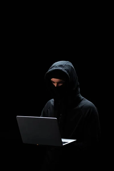 Junge Hacker in Kapuze mit Laptop isoliert auf schwarz — Stockfoto