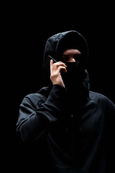 Hacker mit Kapuze und Maske reden auf Smartphone isoliert auf schwarz — Stockfoto