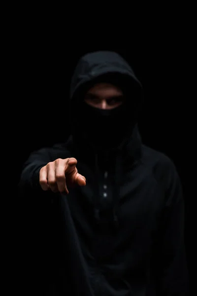 Messa a fuoco selettiva di hacker nel cappuccio che punta con il dito isolato sul nero — Foto stock