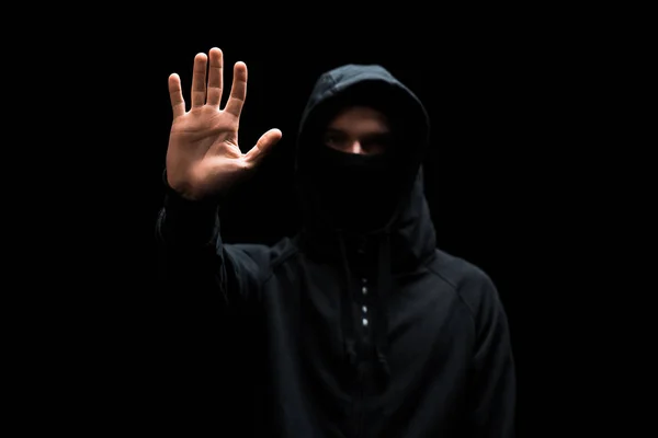 Foco seletivo do hacker anônimo no capuz com a mão estendida isolada no preto — Fotografia de Stock