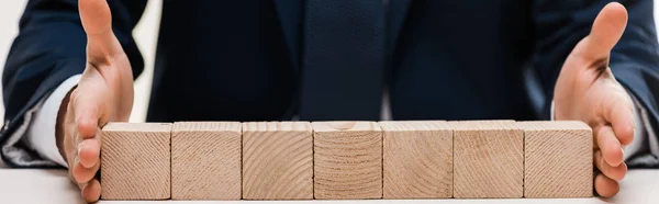 Plano panorámico de hombre de negocios poniendo las manos en la superficie con cubos de madera aislados en blanco - foto de stock