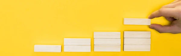 Panoramic shot of man holding wooden block isolated on yellow — Stock Photo