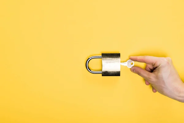 Верхний вид человека касаясь ключа в металлический замок изолирован на желтый — стоковое фото