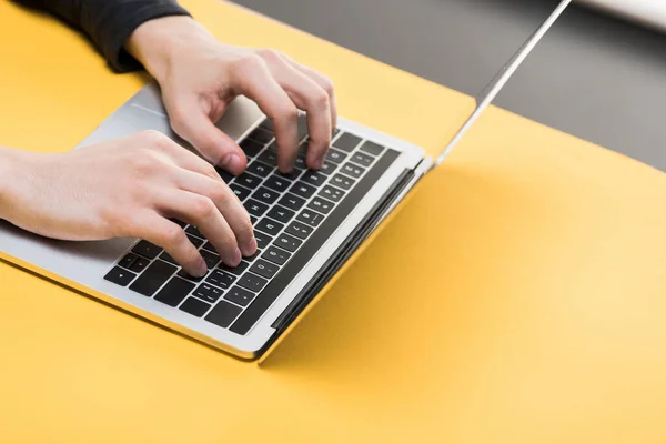 Vista recortada de hacker utilizando el ordenador portátil en el escritorio amarillo - foto de stock