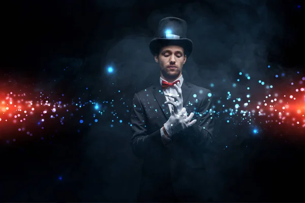 Magician in suit and hat wearing gloves in dark smoky room with glowing illustration — Stock Photo