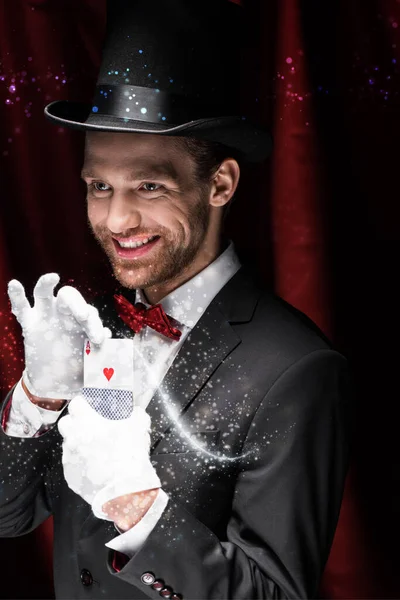 QUIIV, UCRÂNIA - NOVEMBRO 27, 2019: mágico sorridente segurando cartas no circo com cortinas vermelhas e ilustração brilhante — Fotografia de Stock