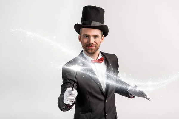 Позитивний фокусник в костюмі і капелюсі тримає паличку ізольовано на сірому з яскравою ілюстрацією — стокове фото