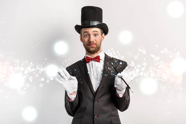 Erwachsener Zauberer mit achselzuckender Geste, Zauberstab auf grau mit leuchtender Illustration — Stockfoto