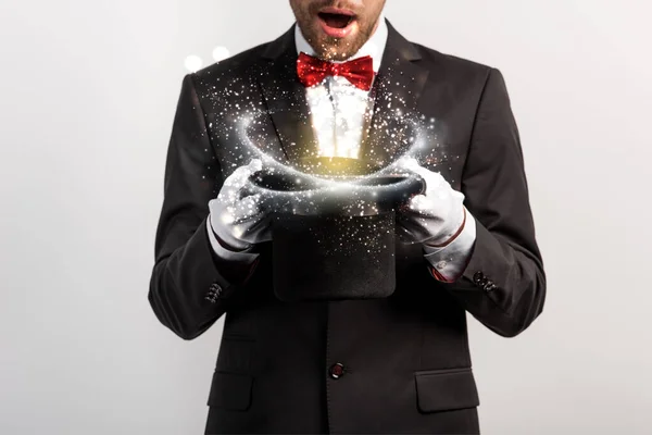 Cropped view of shocked magician holding hat isolated on grey with glowing illustration — Stock Photo