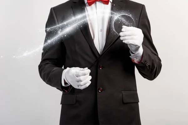 Cropped view of magician in suit and hat holding wand isolated on grey with glowing illustration — Stock Photo