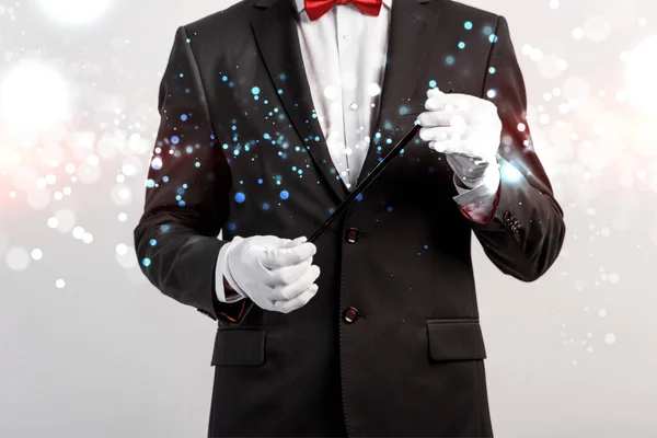 Cropped view of magician in suit and hat holding wand isolated on grey with glowing illustration — Stock Photo