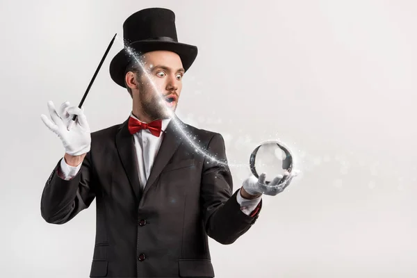Шокований фокусник тримає паличку і магічний м'яч ізольований на сірому з яскравою ілюстрацією — стокове фото