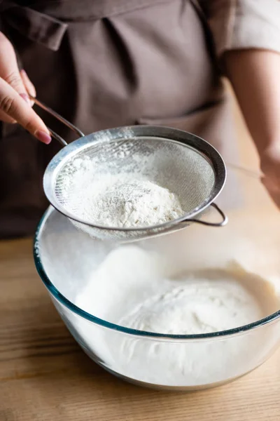 Cropped view of young woman sieving flour in glass bowl — Stock Photo