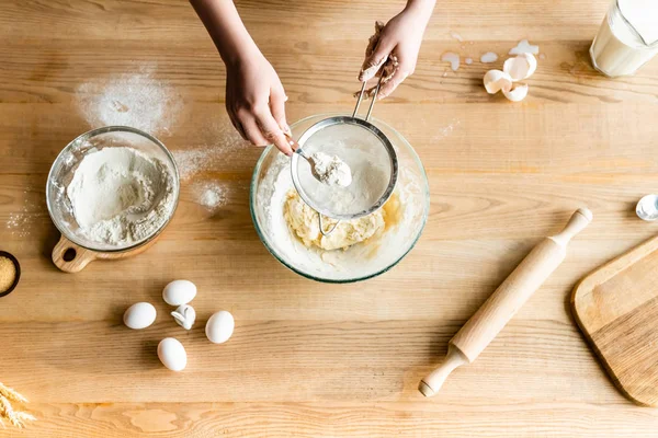 Top view of woman sieving flour into bowl near eggs and figurines with easter bunnies — Stock Photo