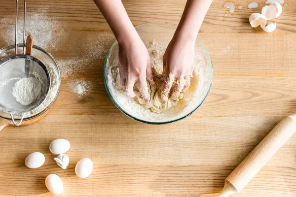 Top view of woman kneading dough near flour in bowl, eggs and figurine with easter bunny — Stock Photo