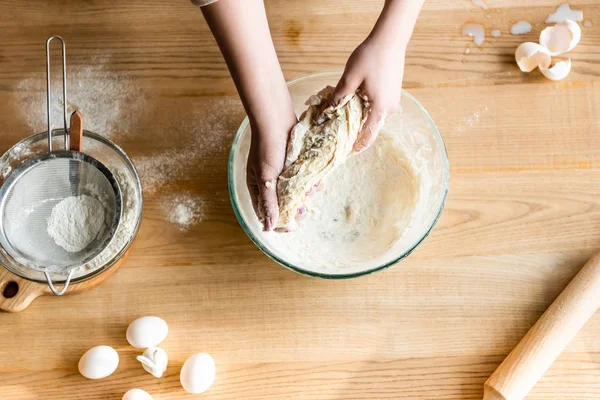 Top view of woman kneading dough near flour in bowl, raw eggs and figurine with easter bunny — Stock Photo