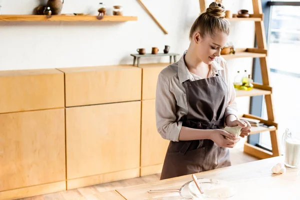 Happy woman in apron holding dough in hands — Stock Photo