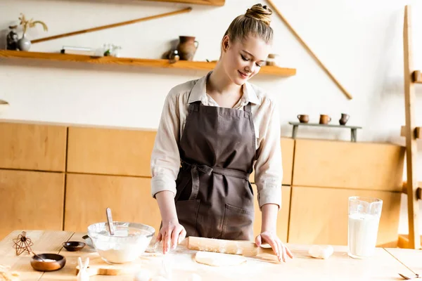 Femme heureuse déroulant la pâte avec rouleau à pâtisserie dans la cuisine — Photo de stock