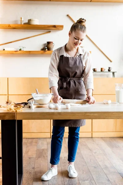 Fröhliche Frau rollt Teig mit Nudelholz neben dekorativen Osterhasen aus — Stockfoto