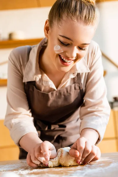 Happy young woman in apron kneading dough — Stock Photo