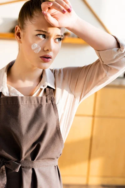 Tired girl with flour on face touching forehead and looking away — Stock Photo
