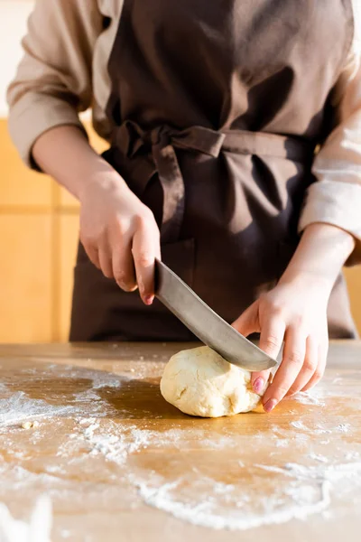 Cropped view of woman cutting dough on wooden table — Stock Photo