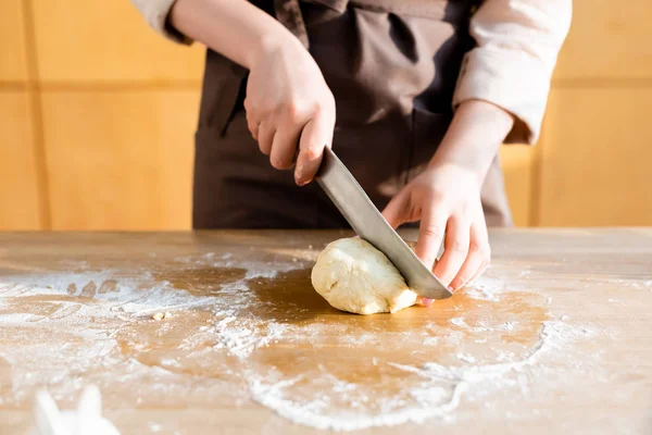 Cropped view of young woman cutting dough on wooden table — Stock Photo