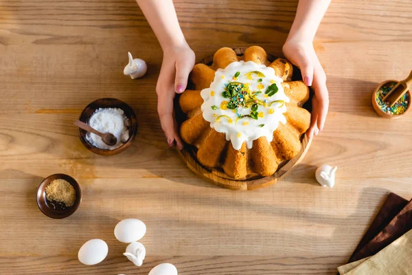 Vista dall'alto della donna che tiene gustosa torta di Pasqua vicino coniglietti pasquali decorativi — Foto stock