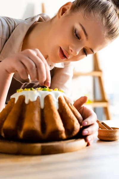 Selective focus of beautiful girl adding sprinkles on tasty easter cake — Stock Photo