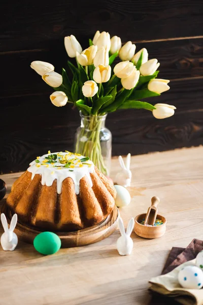 Foco selectivo de delicioso pastel de Pascua cerca de figuritas con conejos de Pascua, huevos pintados y tulipanes - foto de stock