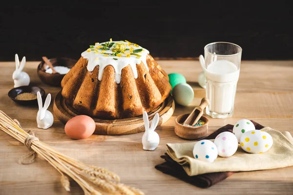 Messa a fuoco selettiva di deliziosa torta pasquale vicino a vetro di latte, figurine con coniglietti pasquali e uova dipinte — Foto stock