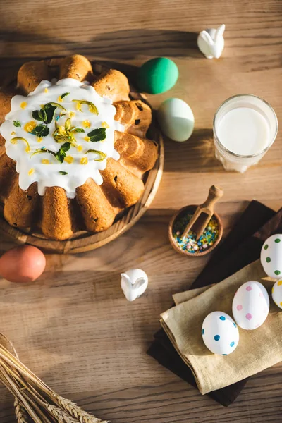 Vista superior de la torta de Pascua cerca del vaso de leche, figuritas con conejos y huevos pintados - foto de stock