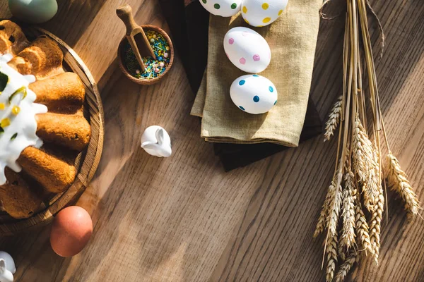 Vista superior de la torta de Pascua cerca de huevos punteados en servilletas de lino, figuritas con conejos y trigo - foto de stock