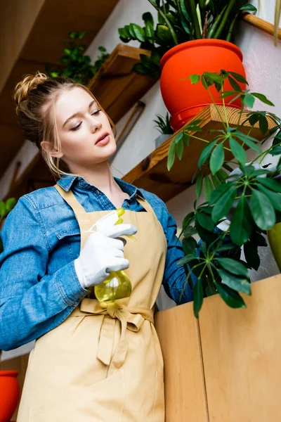 Selective focus of beautiful woman holding spray bottle near green plants — Stock Photo