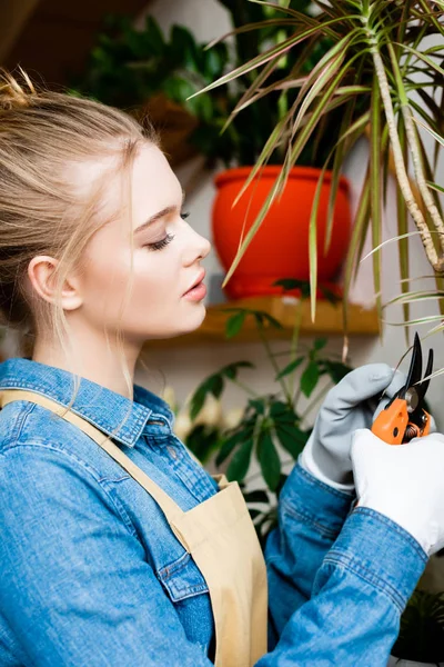 Seitenansicht einer jungen Frau in Handschuhen, die mit der Gartenschere Blätter schneidet — Stockfoto