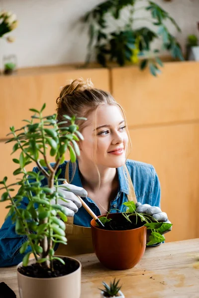 Foyer sélectif de fille heureuse dans des gants tenant la petite pelle tout en transplantant la plante dans le pot de fleurs — Photo de stock