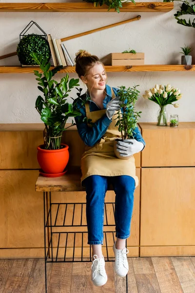 Sonriente joven en delantal sosteniendo planta verde - foto de stock