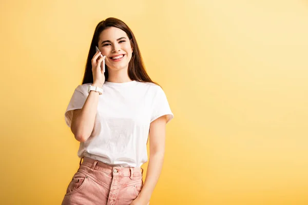 Menina feliz falando no smartphone e sorrindo para a câmera isolada no amarelo — Fotografia de Stock