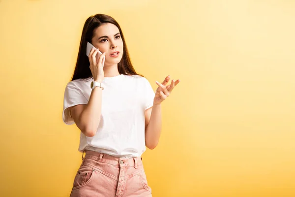 Pensive girl looking away while talking on smartphone isolated on yellow — Stock Photo