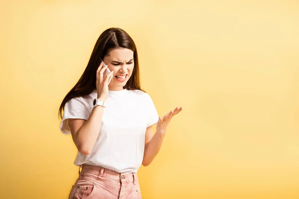 Chica irritada de pie con el brazo abierto y gritando durante la charla en el teléfono inteligente aislado en amarillo - foto de stock