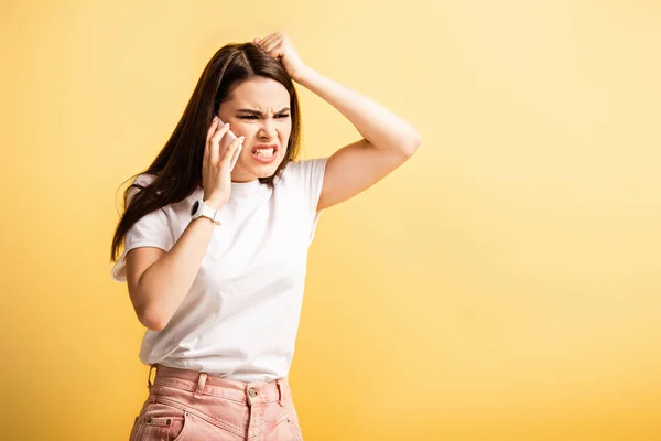 Роздратована дівчина торкається голови і кричить під час розмови на смартфоні ізольовано на жовтому — стокове фото
