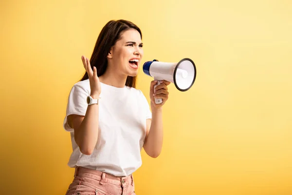 Menina zangada gritando em megafone enquanto olha para o fundo amarelo — Fotografia de Stock