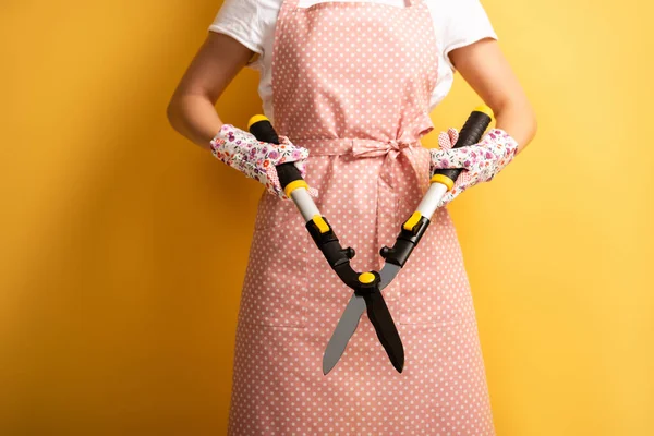 Vista recortada de la mujer en delantal con tijeras de jardinería sobre fondo amarillo - foto de stock